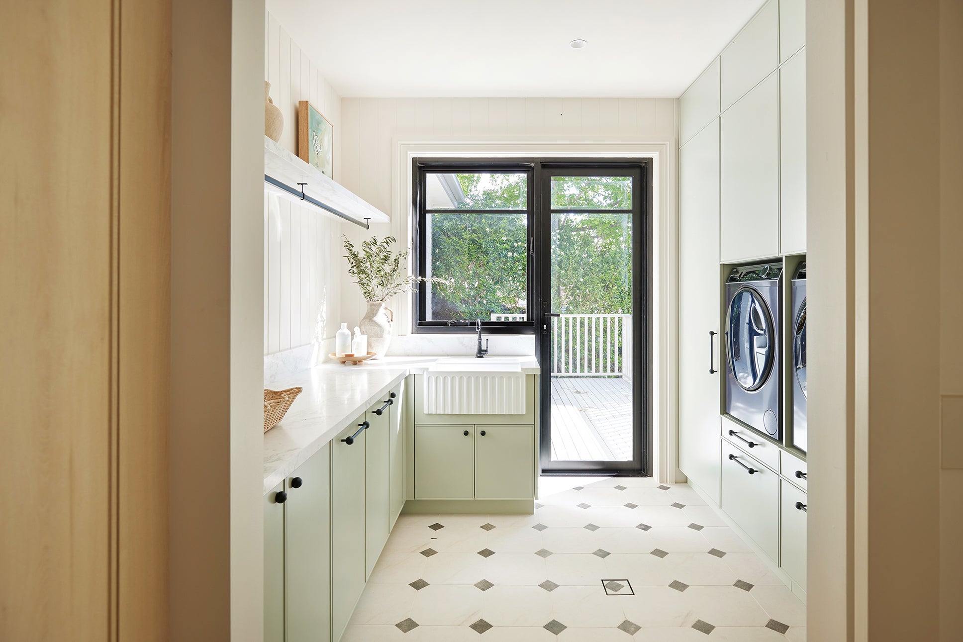 An Urban Farmhouse style laundry with cabochon style tile flooring and green cabinetry 