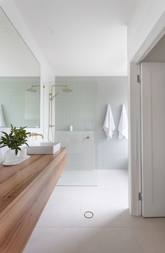 Bathroom with pastel tiles, gold showers and wood countertops